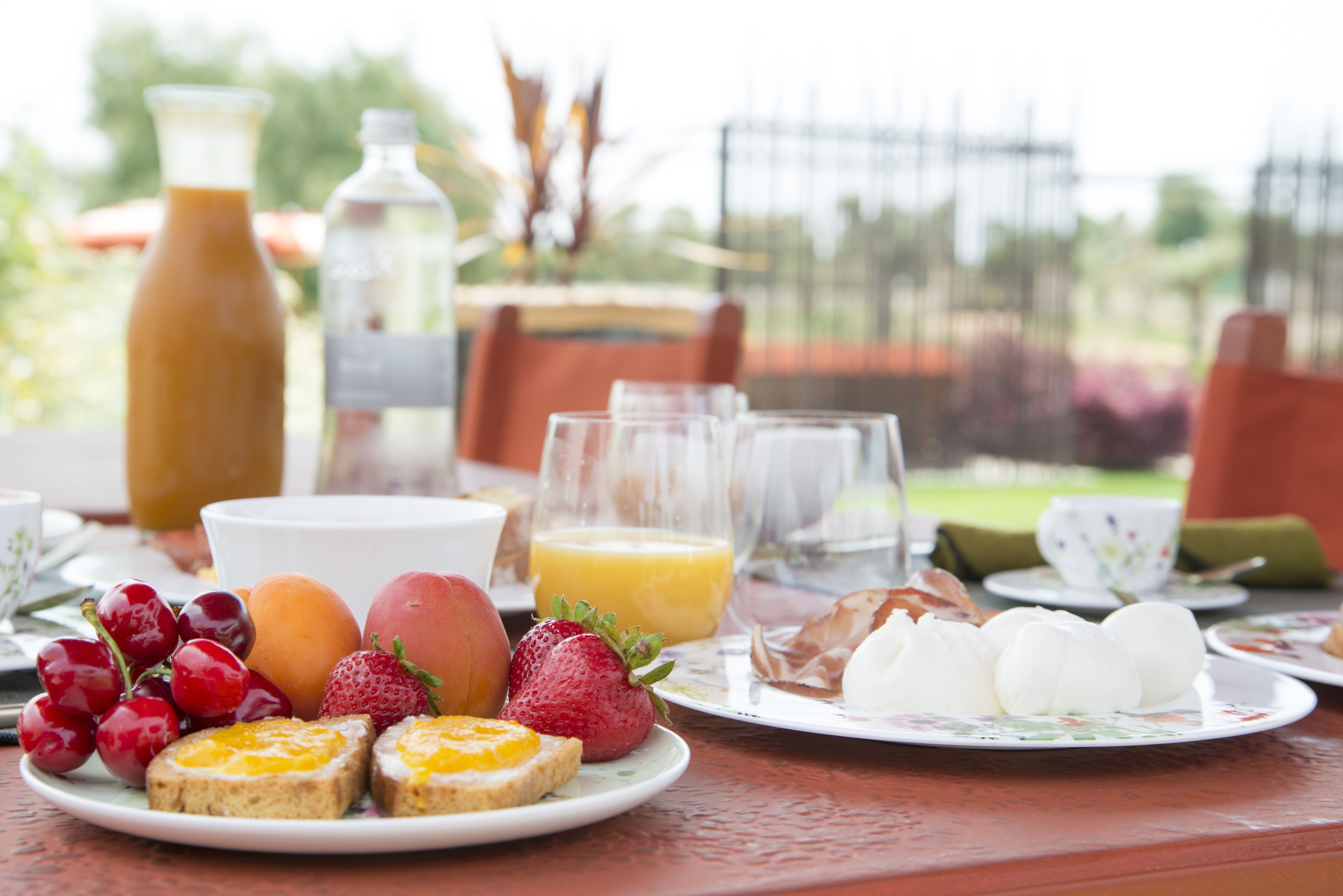 A breakfast table with plates of toast, fruit, and eggs, along with a bottle of juice and a pitcher.
