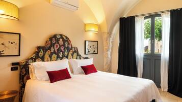 Una cama bien tendida con ropa de cama blanca y roja, un cabecero decorativo y una ventana con cortinas negras.