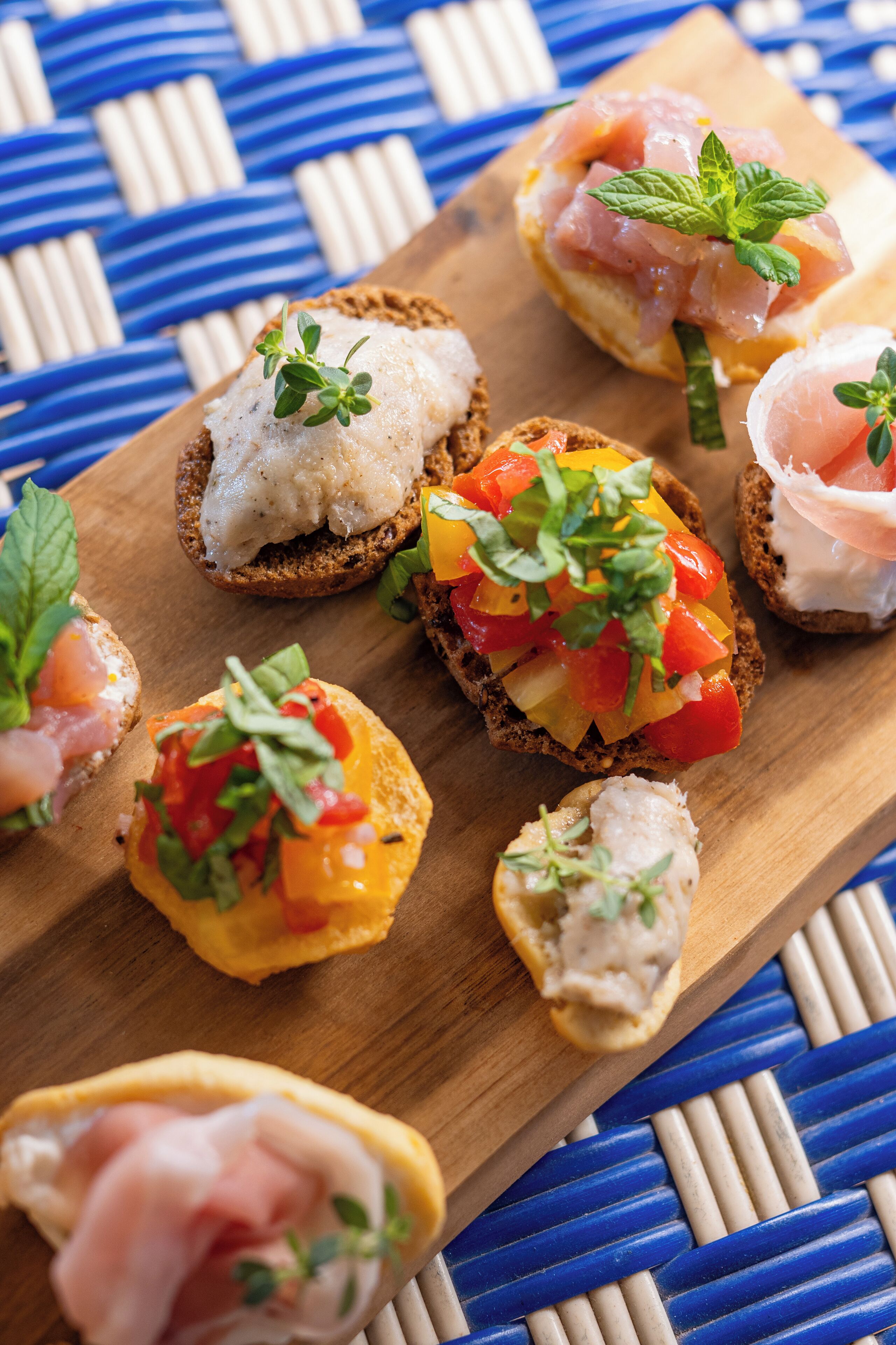 A wooden board with various appetizers, including bruschetta with tomatoes and herbs, and other small dishes with different toppings.