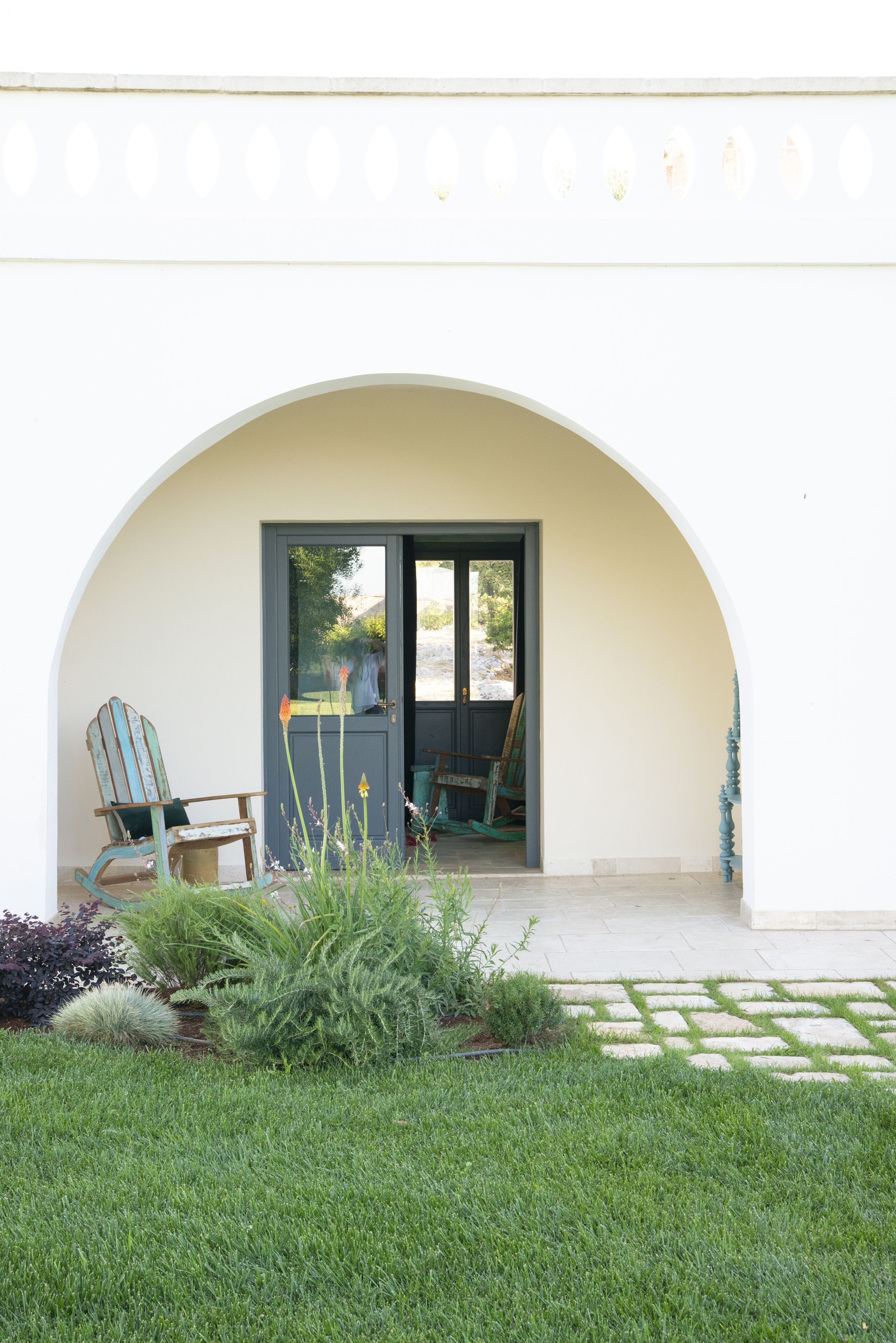 Varanda coberta com porta que dá para um jardim. Duas cadeiras e uma mesa são visíveis.