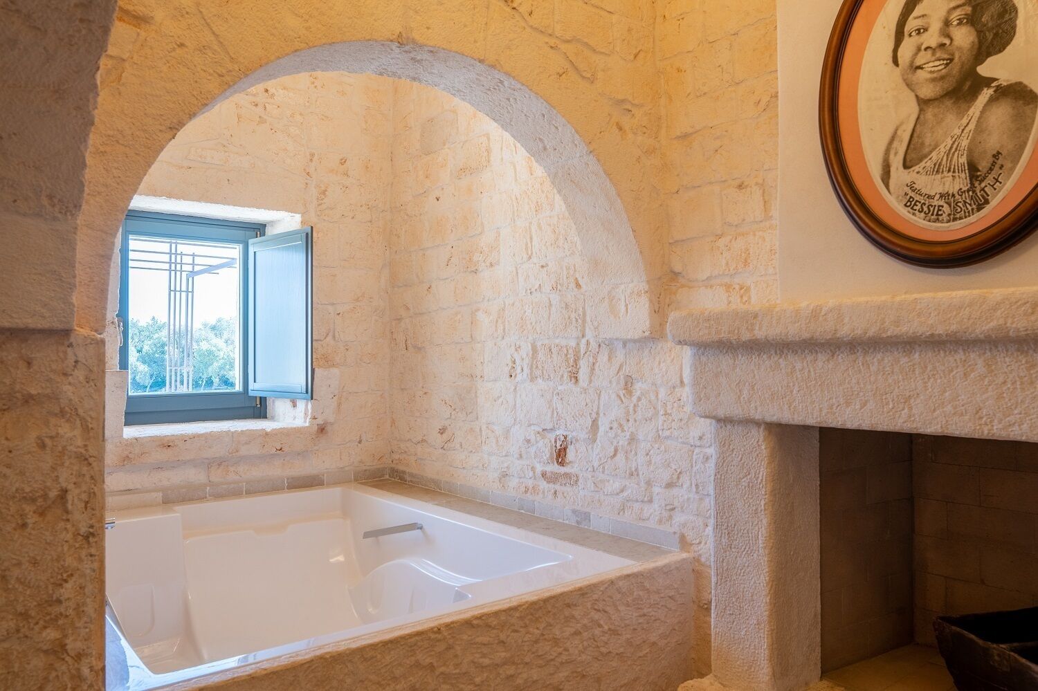 A bathroom with a bathtub, an arched window, and a framed picture on the wall.