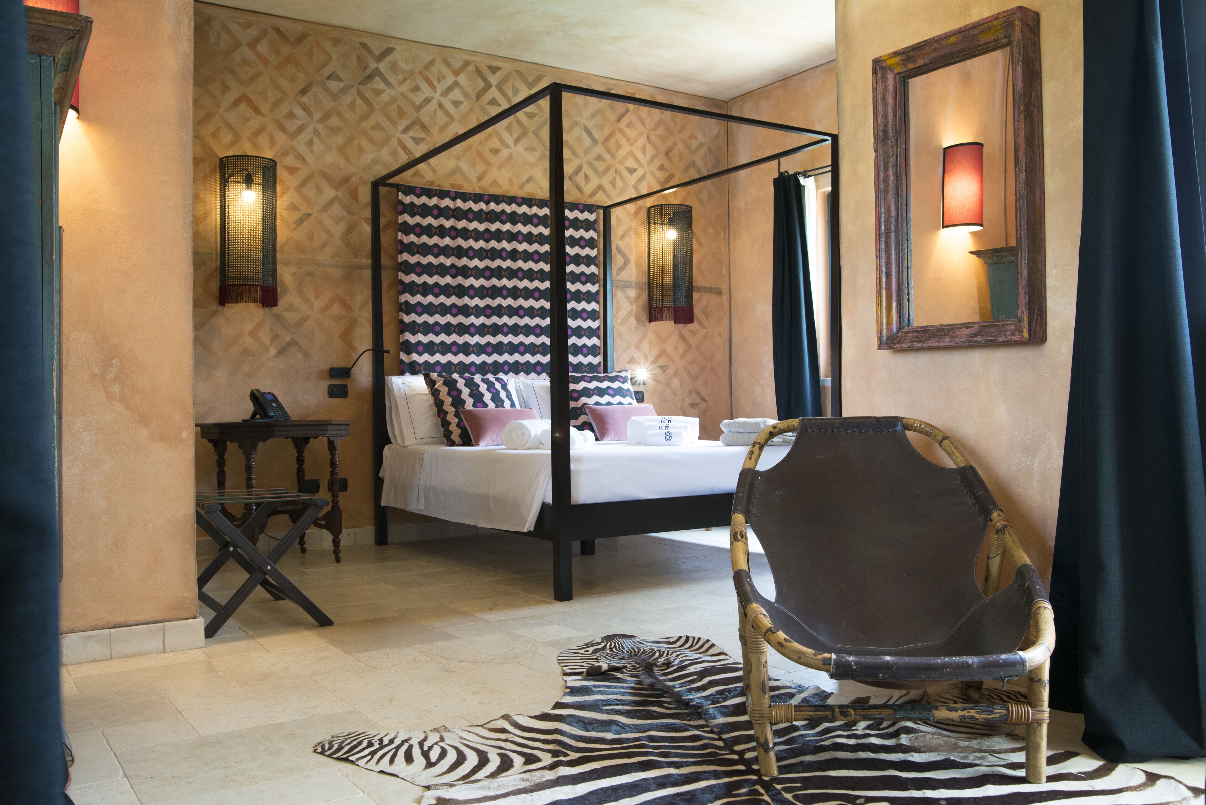 Una cama con dosel, un tapete con estampado de cebra, una silla de madera y apliques de pared.