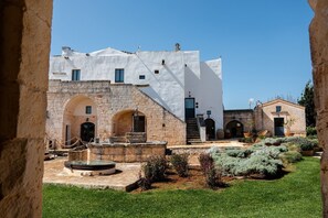 A courtyard with a white building, stone arches, and a fountain. - Masseria Santo Scalone (Ostuni)