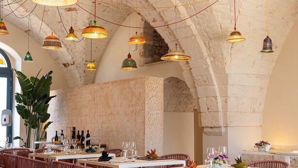 Ein Restaurant mit rustikalen Steinwänden, hängenden Pendelleuchten und Korbmöbeln.