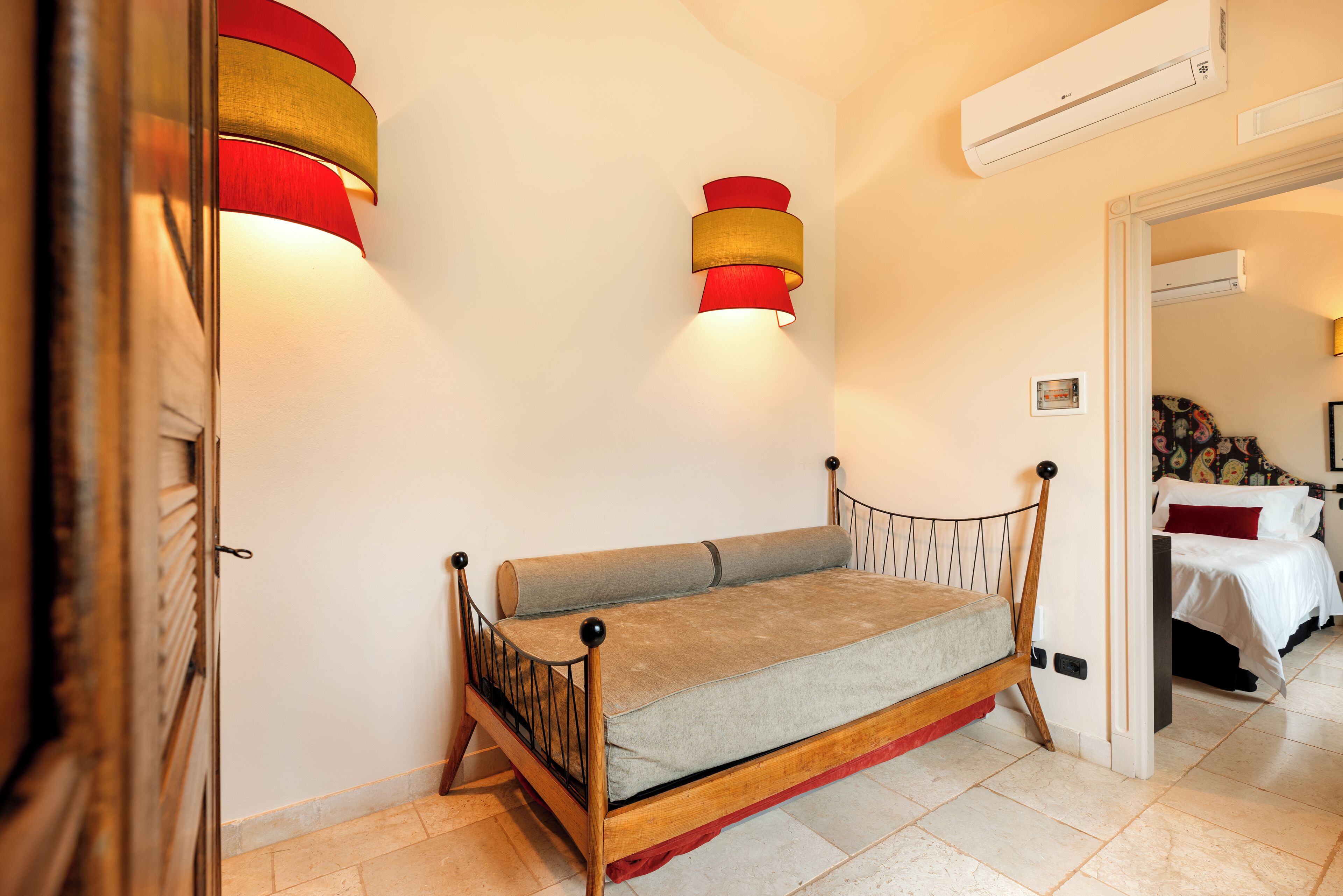 Un dormitorio con una cama de madera, una lámpara de pared roja y dorada, y un aire acondicionado blanco.