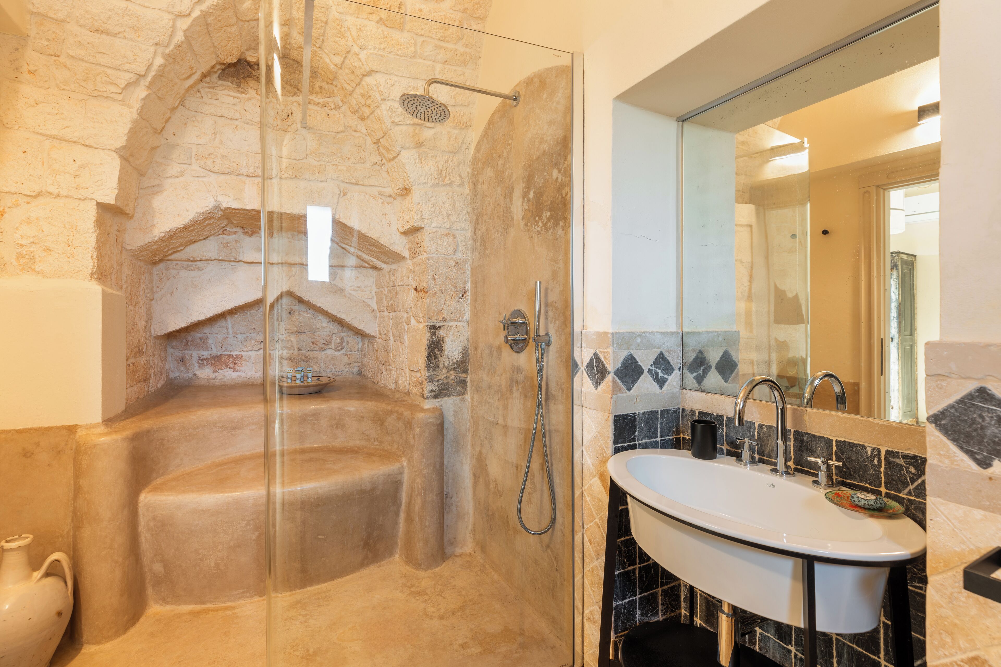 A bathroom with a stone sink, a glass-enclosed shower, and a tiled wall.