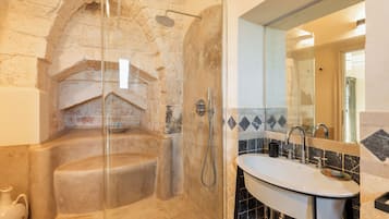 Un baño con un lavamanos de piedra, ducha con cerramiento de vidrio y pared con azulejos.