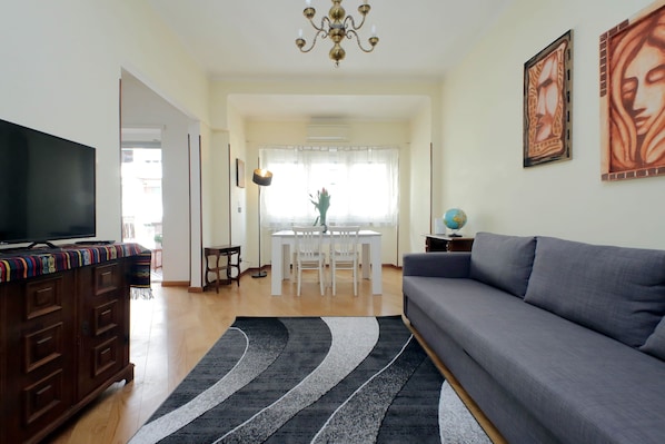 A living room with a sofa, TV, wooden cabinet, and a dining area with a table and chairs.