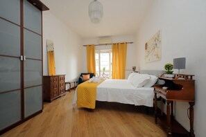 A hotel room with a bed, a wooden desk, a dresser, a mirror, and a window with curtains.