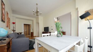 A modern living room with a white dining table, grey sofa, and a chandelier.