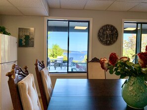 Un comedor con vistas al mar, un reloj en la pared y un jarrón con flores sobre la mesa.