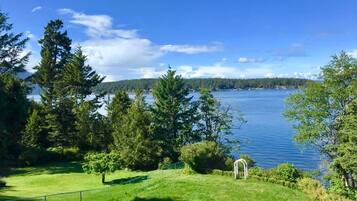 Ein grünes Rasenstück mit einem befestigten Weg, der zu einer kleinen weißen Laube mit Blick auf einen See führt.