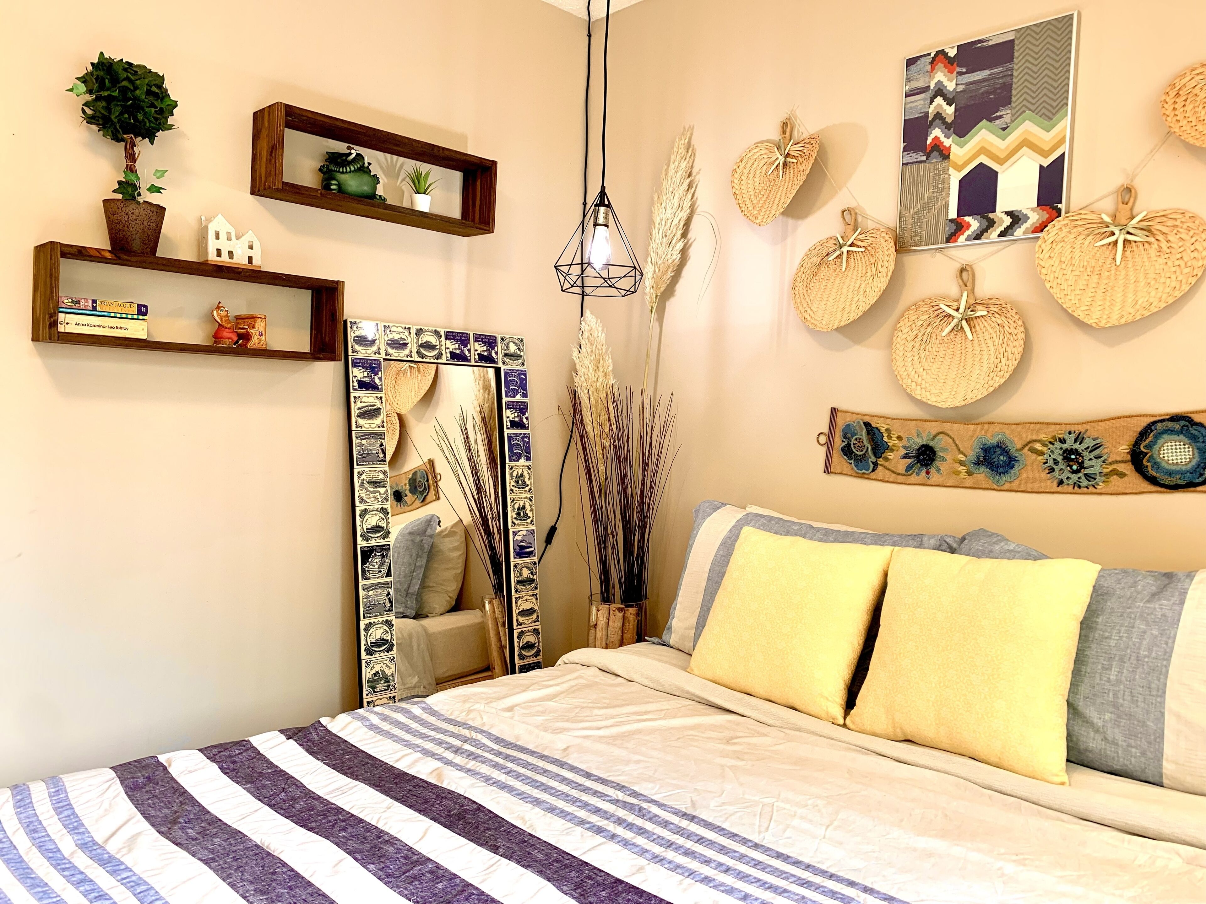 A bedroom with a bed, a bedside table, a mirror, shelves with decorative items, and a wall with various wall art.