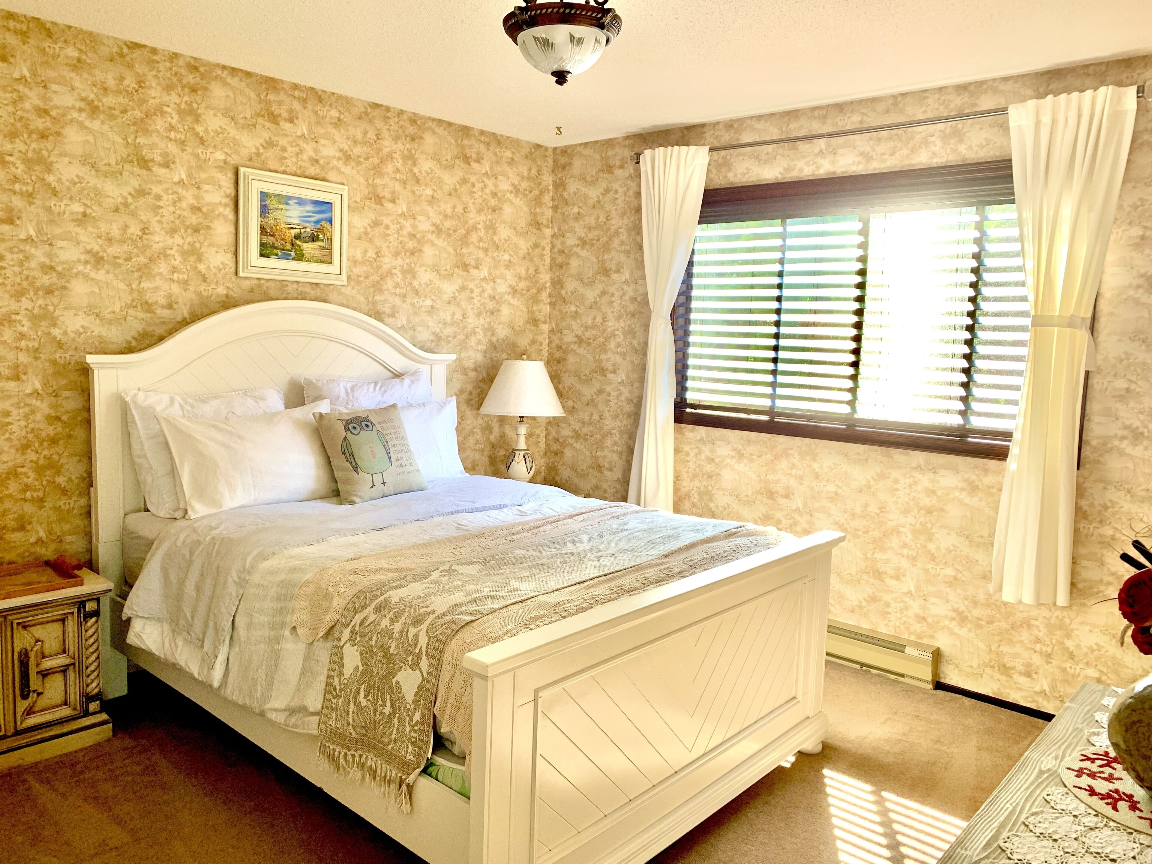 A neatly arranged bedroom with a bed, bedside lamp, and a window with curtains.