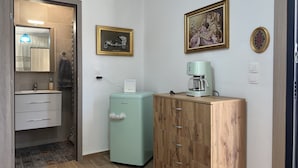 Ein gemütlicher Raum mit einem Holzschrank, einem kleinen Kühlschrank, einer Kaffeemaschine und einem Spiegel, an dem ein Handtuch hängt.