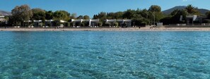 A coastal hotel with beach access, clear blue waters, and a mountainous backdrop.