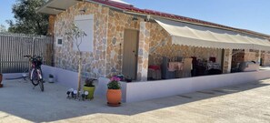 A stone building with a covered patio area, a bicycle, and potted plants.