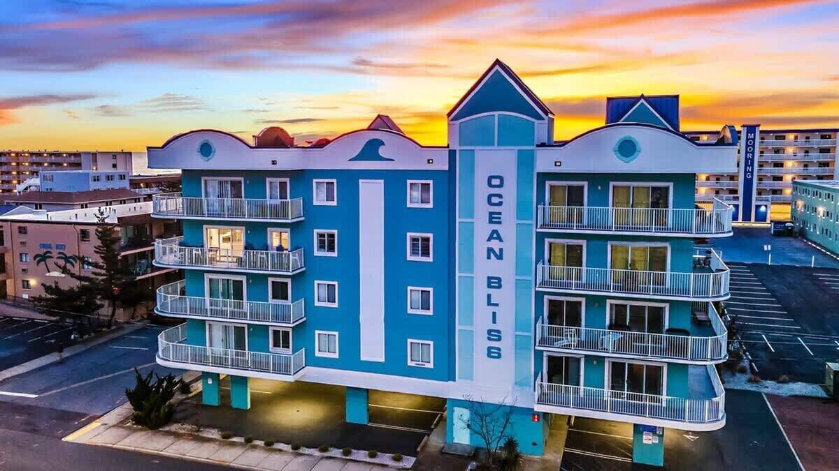 A multi-story hotel with balconies, a prominent 'Ocean Bliss' sign, and a parking lot in the foreground.