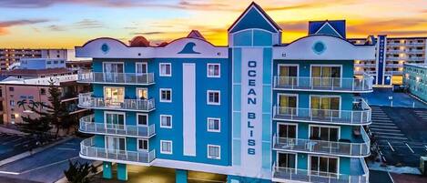 A multi-story hotel with balconies, a prominent 'Ocean Bliss' sign, and a parking lot in the foreground.