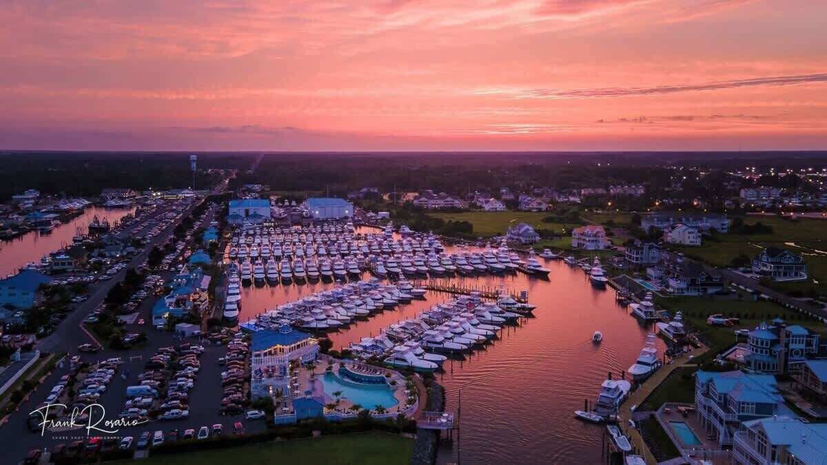 Ein Yachthafen mit zahlreichen Booten, ein großes Gebäude mit Schwimmbad und eine Wohngegend mit Häusern.