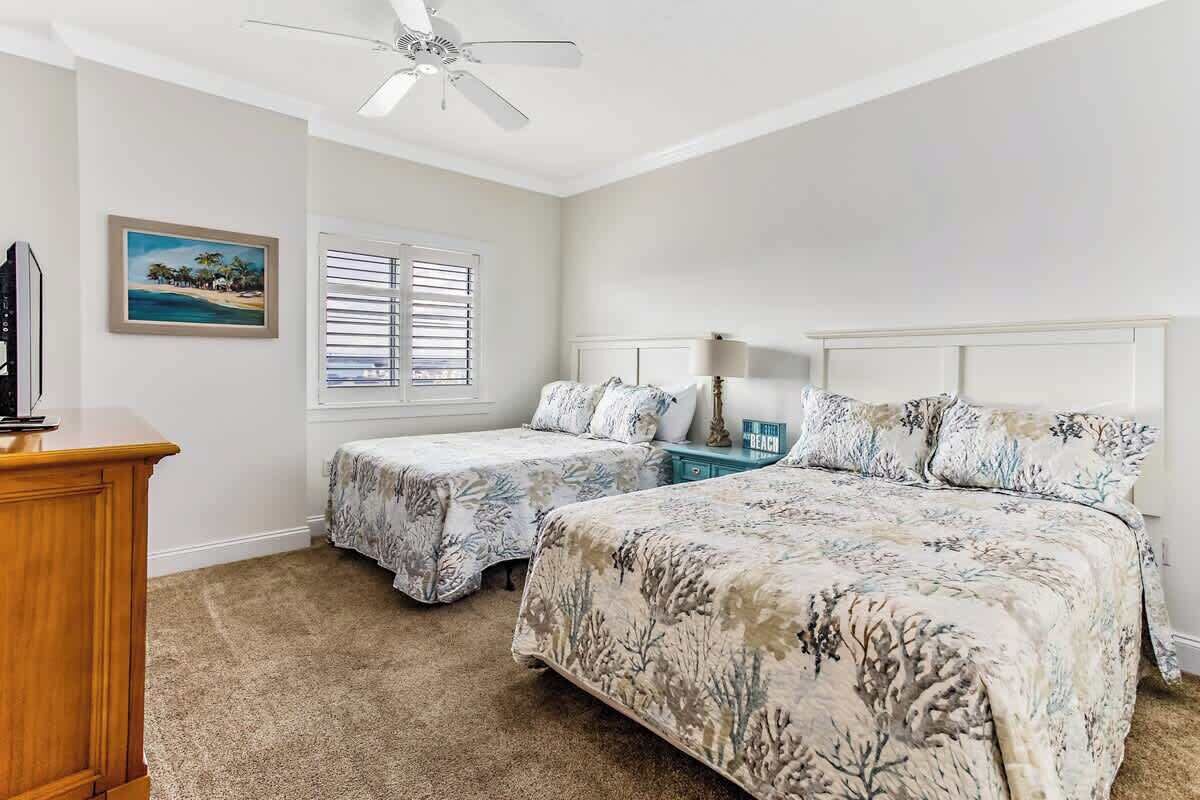 A bedroom with two beds, a ceiling fan, a TV, and a beach-themed painting.