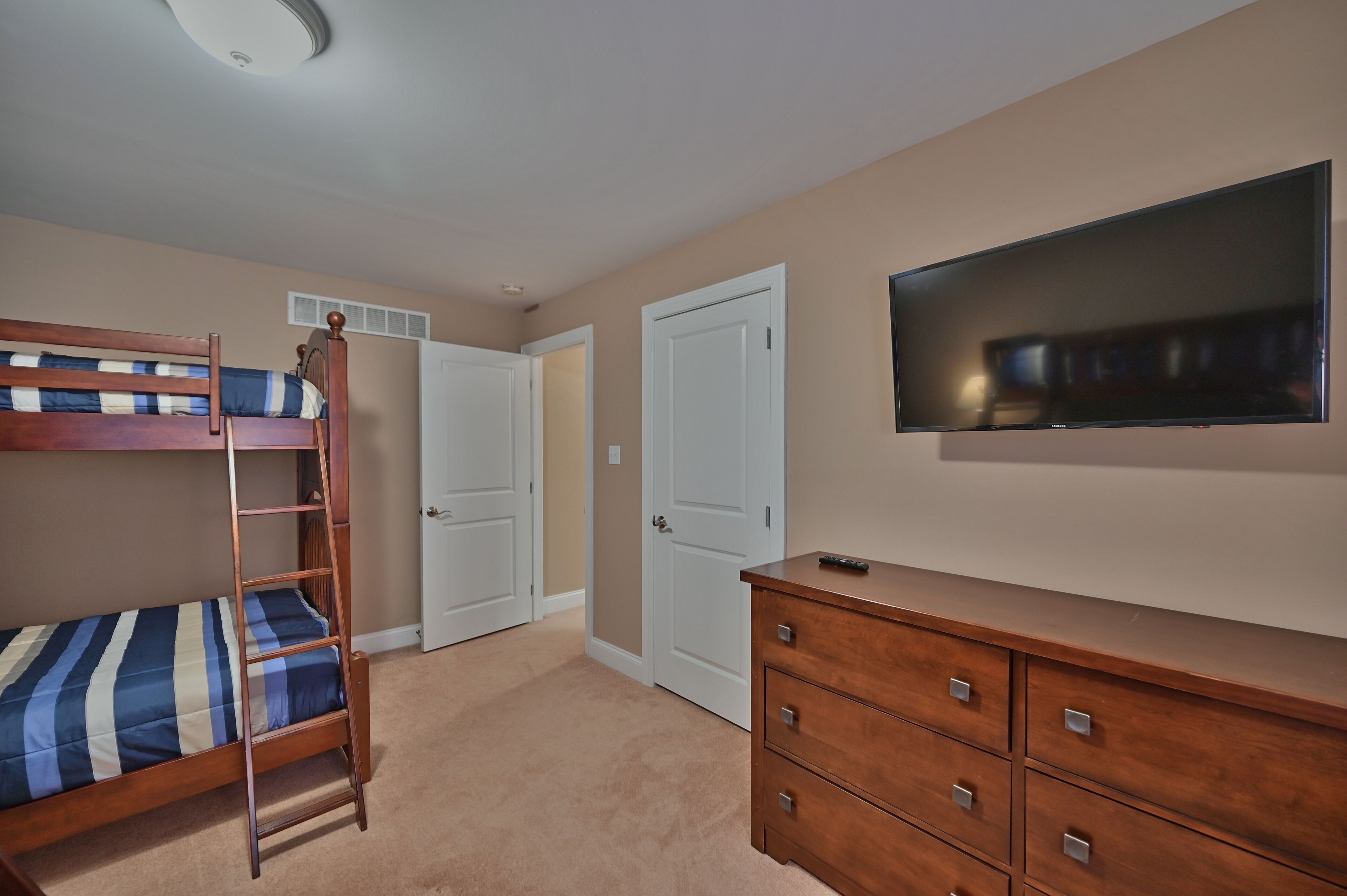 A bedroom with a bunk bed, a dresser, a television, and a door.