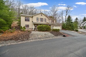 A two-story house with a front porch, a driveway, and a landscaped front yard with trees and shrubs.