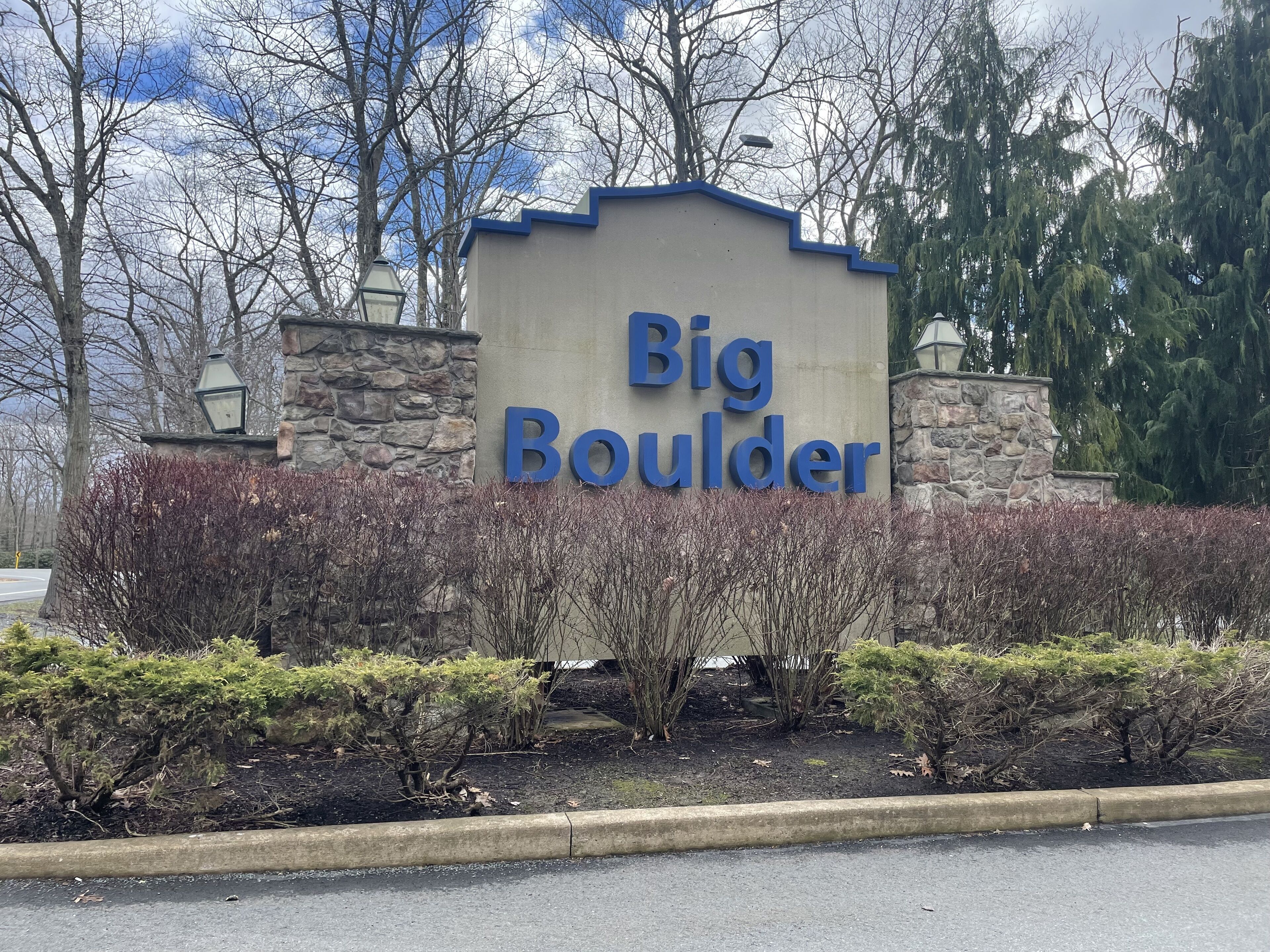 A sign for Big Boulder with a stone wall and shrubbery in front.