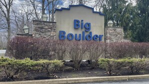 Un panneau indiquant l’emplacement de Big Boulder, avec un mur de pierres et des arbustes devant.