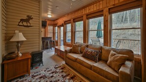 L’intérieur chaleureux d’un chalet avec un plafond en bois, un canapé en cuir, une cheminée et de grandes fenêtres donnant sur le paysage extérieur.