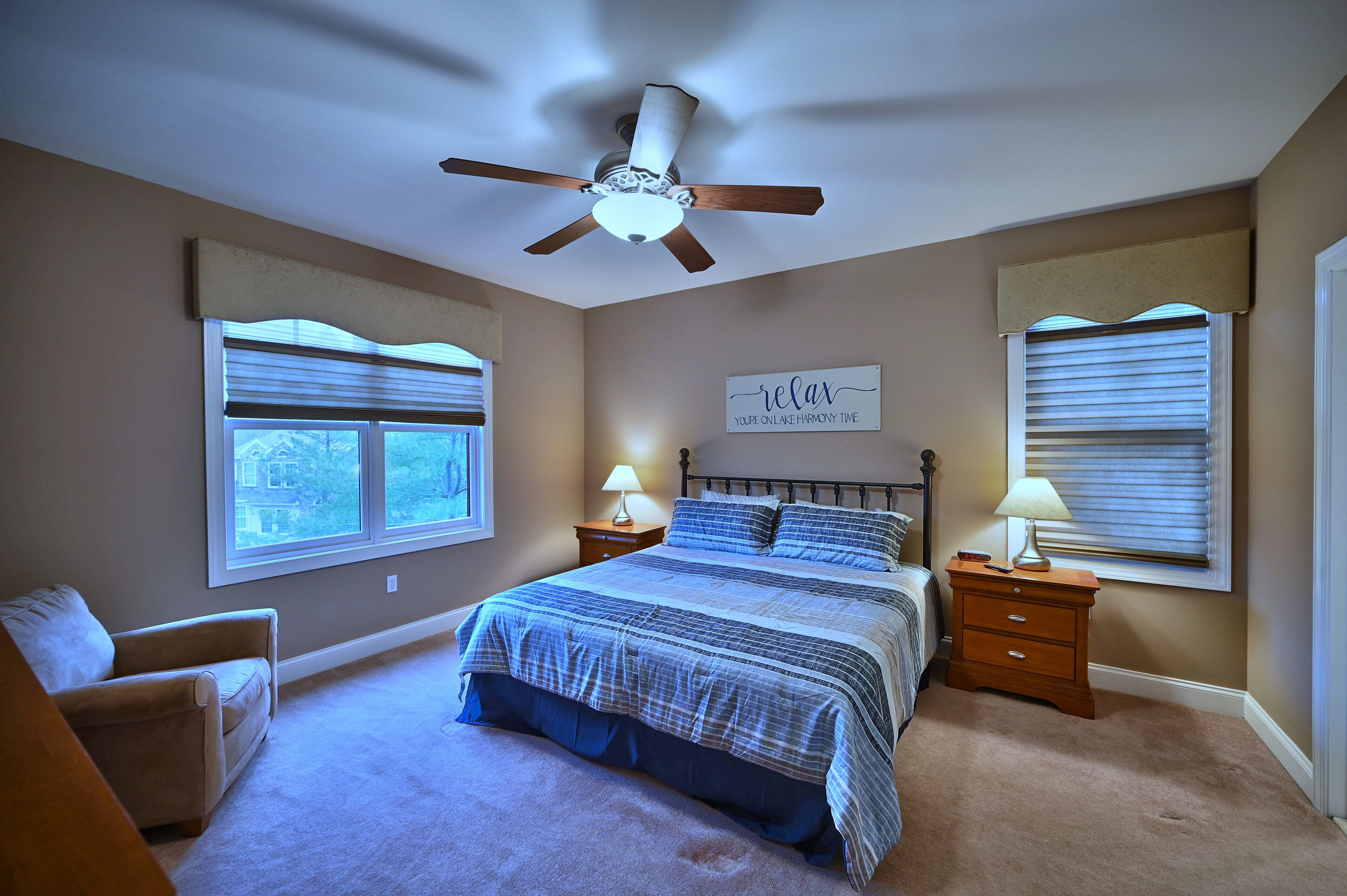 A bedroom with a bed, two bedside tables, a ceiling fan, and a wall sign.