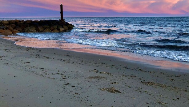 A beach with a rocky breakwater and waves.