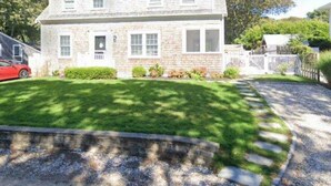 A two-story stone house with a front porch, a visible garage, and a well-maintained lawn.