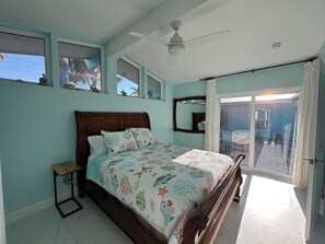 A bedroom with a bed, a ceiling fan, a window, and a sliding glass door leading to an outdoor area.