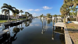 A calm canal with boats docked, surrounded by palm trees and residential buildings.