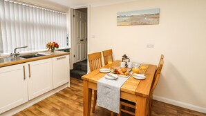 A dining area with a wooden table set for breakfast, including croissants, juice, and coffee. A kitchen with white cabinets and a sink is visible in the background. - Station View (Whitby)