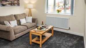 A living room with a beige sofa, a wooden coffee table, a lamp, and a window with a view of buildings. - Station View (Whitby)