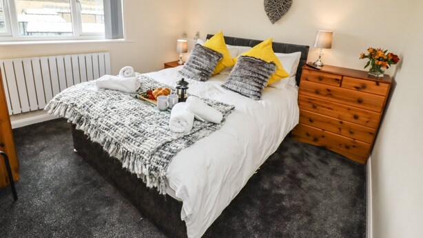 A bedroom with a bed, bedside tables, a dresser, a chandelier, and a window. - Station View (Whitby)