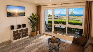 A living room with a large window, a television, a plant, and a sofa. - Beautiful apartment directly on the beach Living room and terrace with panoramic sea view     (Heiligenhafen)