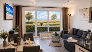 A modern living room with a dining area, large windows with a view of the beach, a sofa, and a coffee table. - Beautiful apartment directly on the beach Living room and terrace with panoramic sea view     (Heiligenhafen)