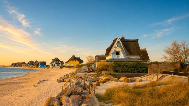 A coastal village with traditional houses, a sandy beach, and a rocky shoreline. - Beautiful apartment directly on the beach Living room and terrace with panoramic sea view     (Heiligenhafen)