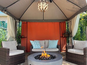 A covered outdoor seating area with wicker furniture and a central fire pit.