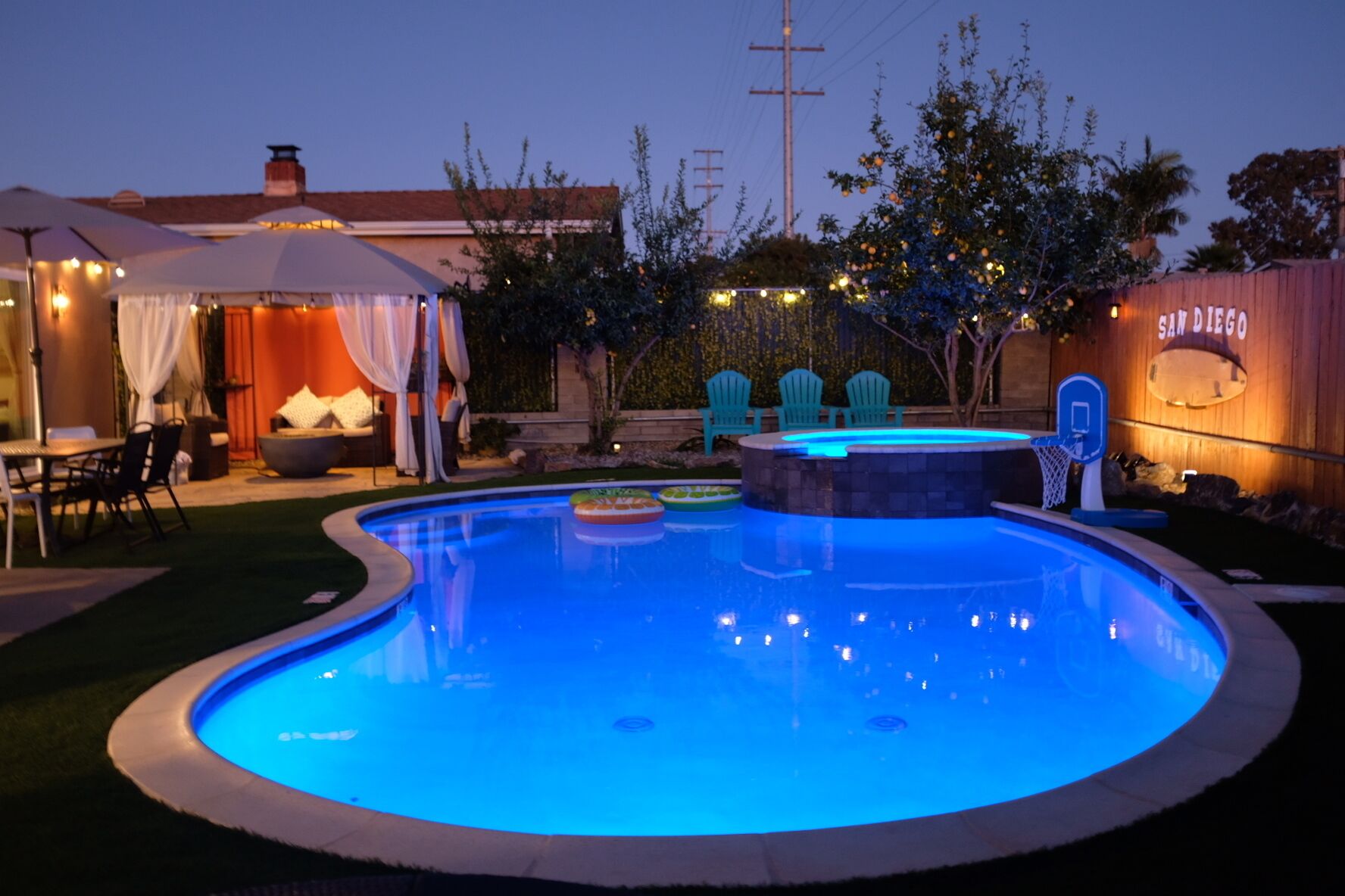 Une piscine à bord incurvé, entourée d’un patio aménagé avec des meubles d’extérieur et des guirlandes lumineuses.