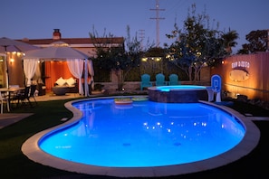 A swimming pool with a curved edge, surrounded by a patio area with outdoor furniture and string lights.