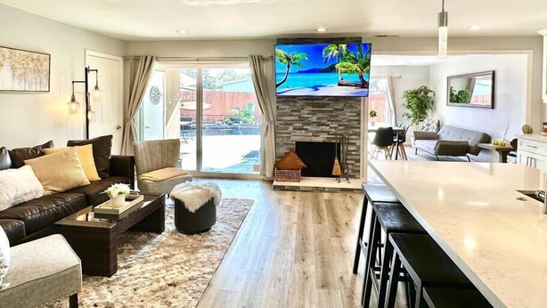 A modern living room with a fireplace, a large TV, and a dining area with a bar. - Prime Location: Lux 4BR w Pool/Spa/Cabana/Firepit (San Diego)