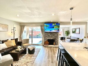A modern living room with a fireplace, a large TV, and a dining area with a bar. - Prime Location: Lux 4BR w Pool/Spa/Cabana/Firepit (San Diego)