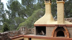Fornera exterior de pedra i rajol amb xemeneia, envoltada d'arbres.