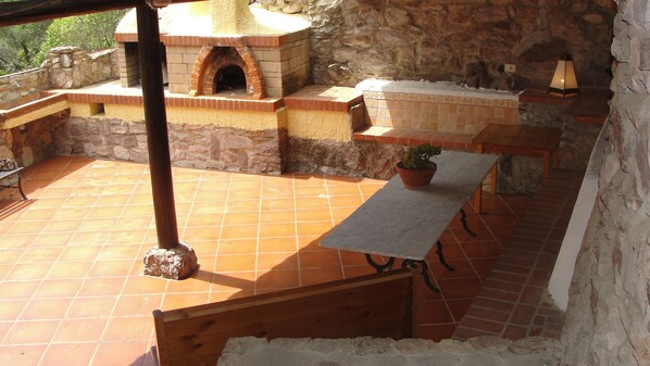 Une terrasse extérieure dotée d’un four en briques, de murs en pierre et d’un sol carrelé.