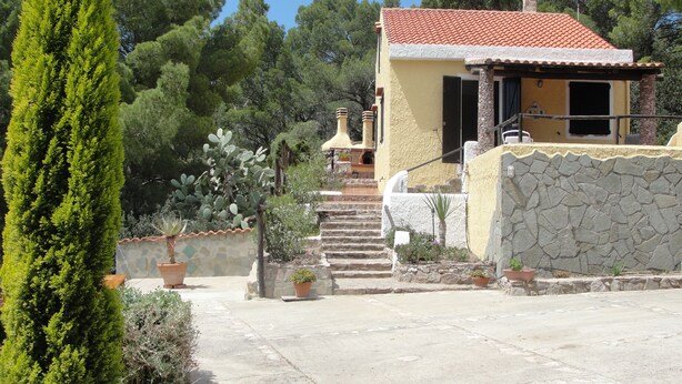 Edifici d'estil mediterrani amb façana de pedra, teulada vermella i una escala que condueix a una porta.