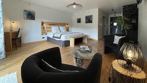 A modern bedroom with a wooden headboard, a large bed, a glass coffee table, and a black armchair. - Le Volcans des Sens (Torsiac)